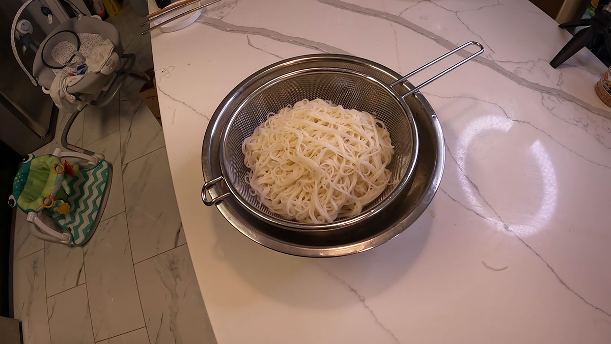 Somen noodles placed on top of a colander with ice and bowl at the bottom 