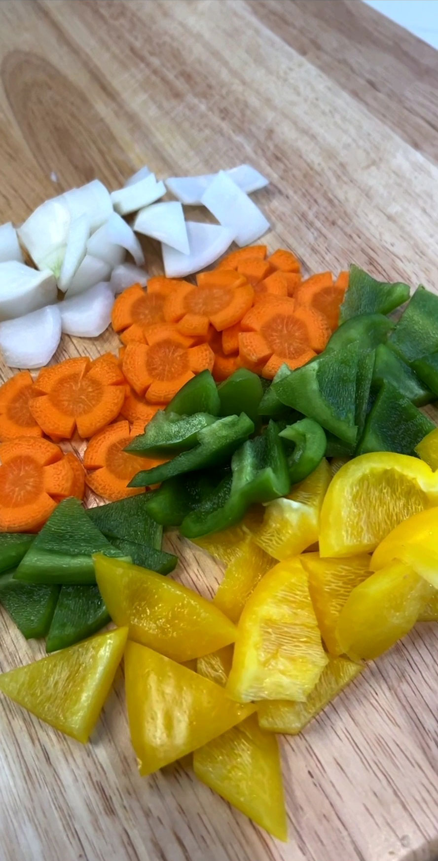 Onions, carrots, green and yellow peppers cut up and placed on top of the chopping board 
