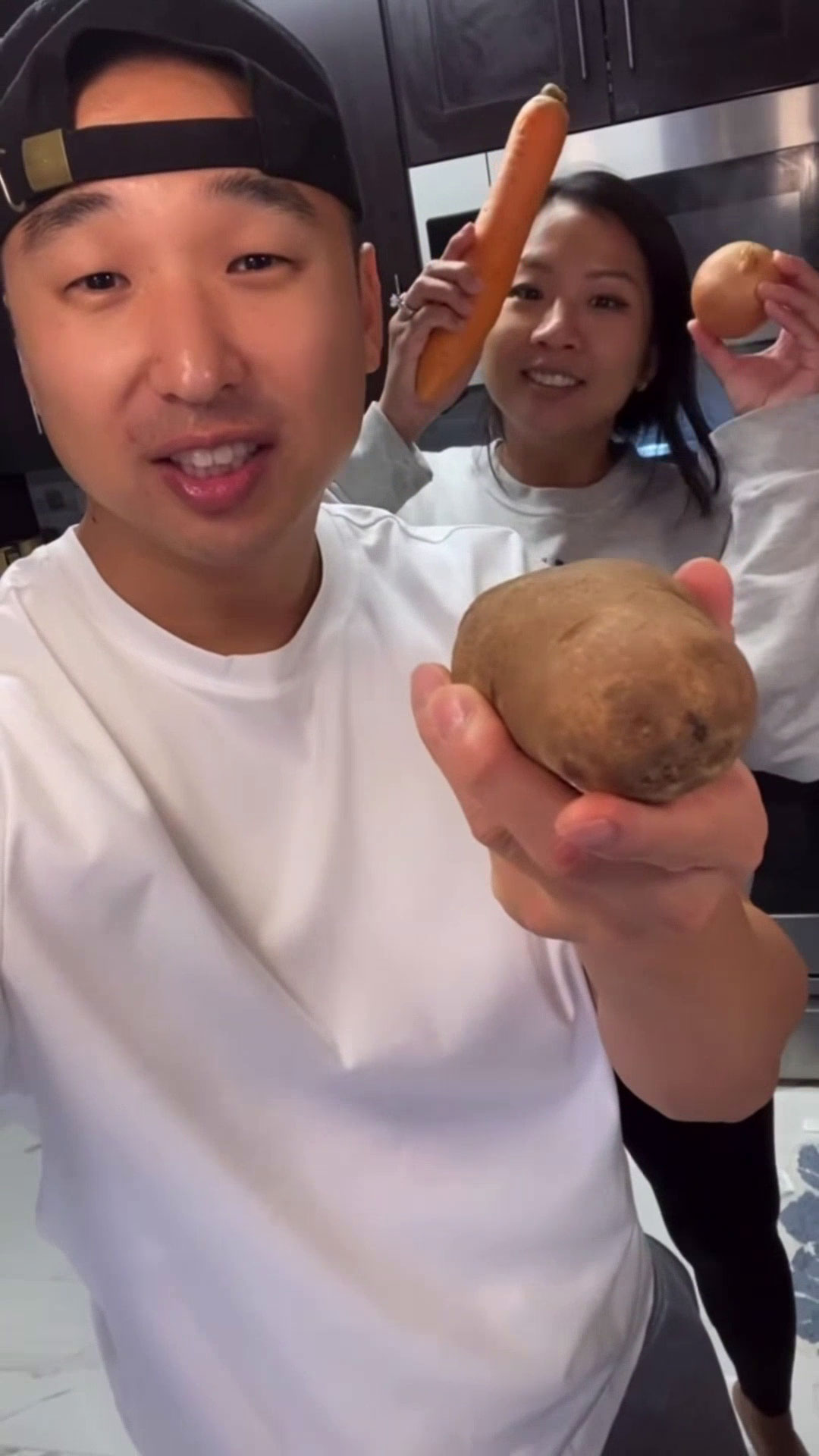 Chef Chris Cho and his wife holding potatoes, carrots, and onions