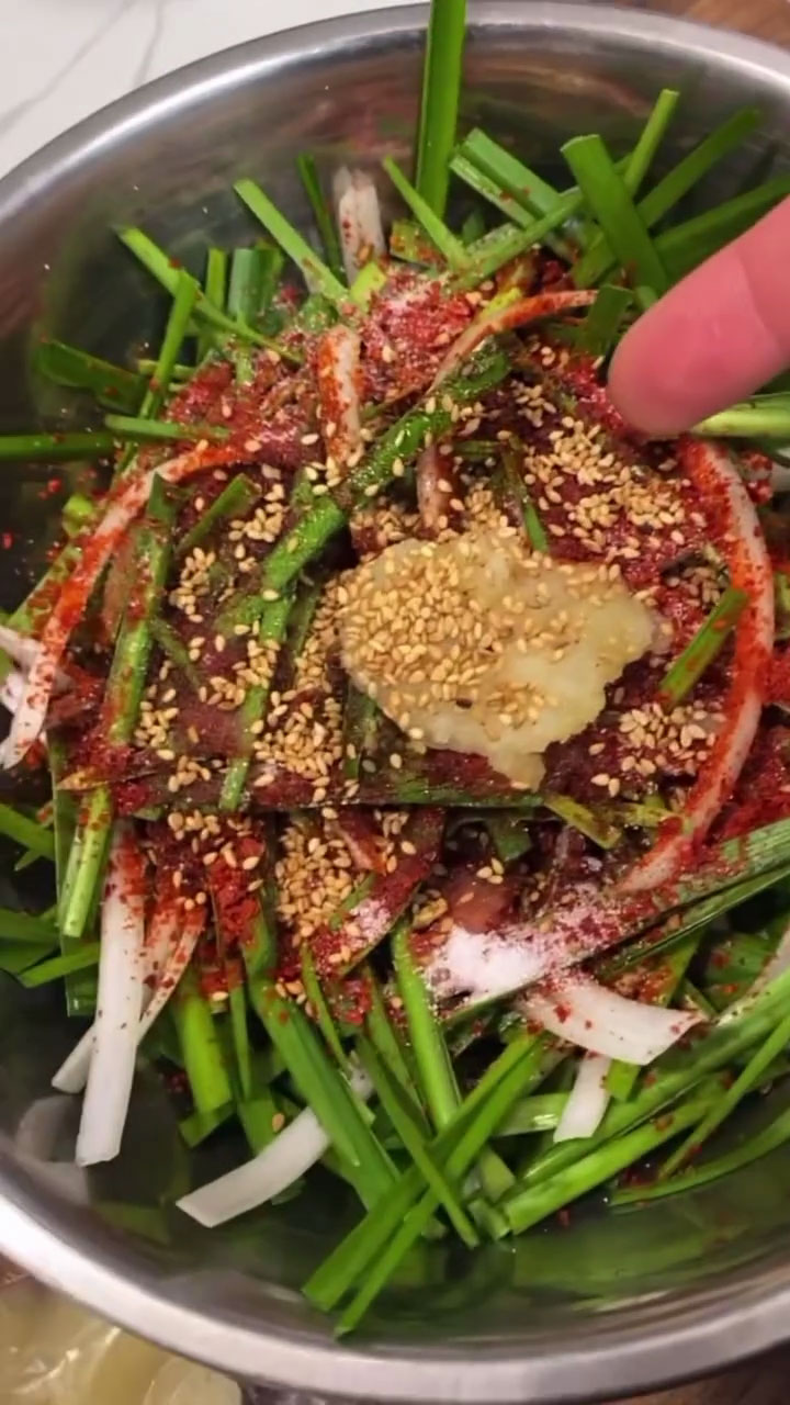 Season the chives with gochugaru, soy sauce, vinegar, sugar, mirin, garlic, sesame oil, and sesame seeds 